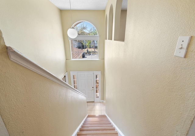 stairway featuring baseboards, a towering ceiling, tile patterned flooring, and a textured wall