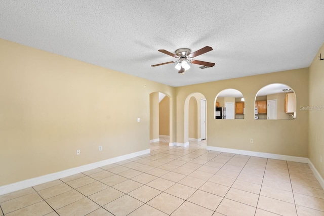 unfurnished room featuring light tile patterned floors, baseboards, arched walkways, ceiling fan, and a textured ceiling