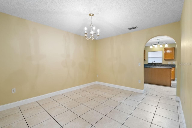 empty room with visible vents, a sink, arched walkways, an inviting chandelier, and light tile patterned floors