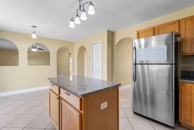 kitchen with dark stone countertops, light tile patterned floors, freestanding refrigerator, pendant lighting, and a center island