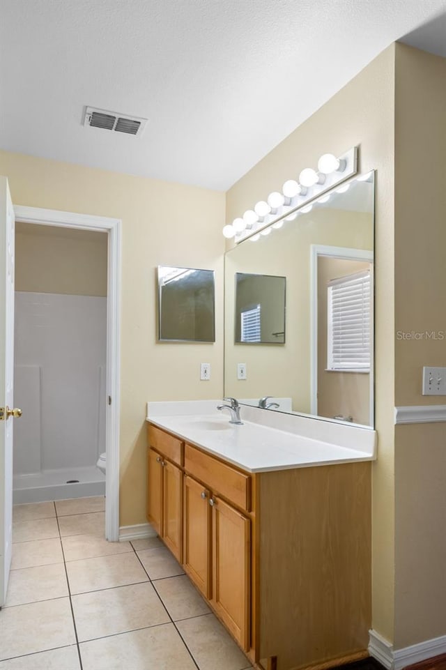 full bath featuring tile patterned flooring, visible vents, baseboards, walk in shower, and vanity