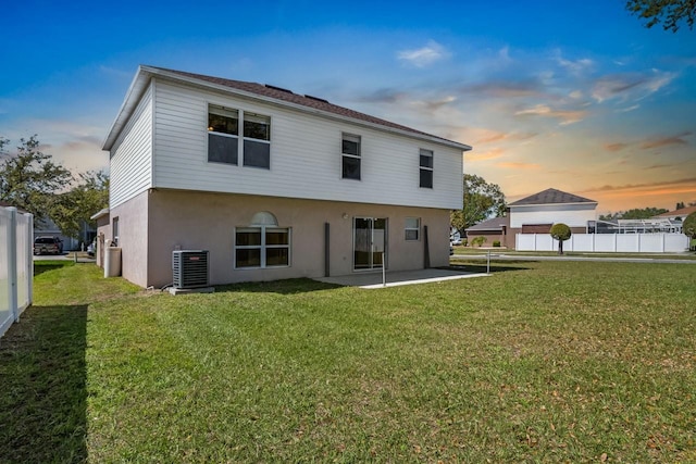 back of house at dusk with fence, stucco siding, cooling unit, a yard, and a patio area