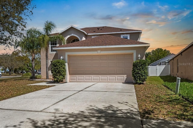 traditional-style home featuring fence, roof with shingles, driveway, stucco siding, and a garage