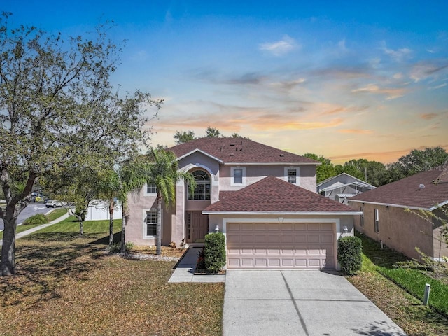 traditional home with roof with shingles, an attached garage, a yard, stucco siding, and concrete driveway