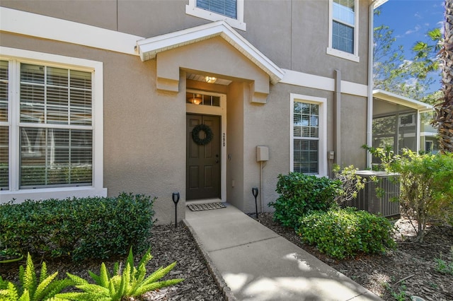 view of exterior entry with central AC unit and stucco siding