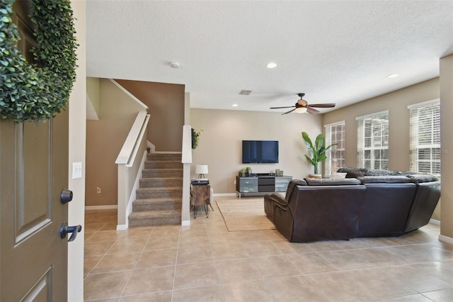 living area with visible vents, a textured ceiling, stairway, light tile patterned flooring, and ceiling fan