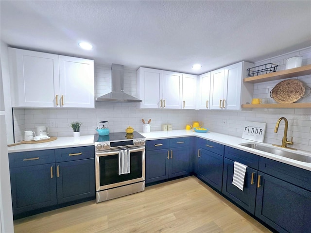 kitchen featuring a sink, stainless steel range with electric stovetop, blue cabinets, wall chimney exhaust hood, and light wood-type flooring