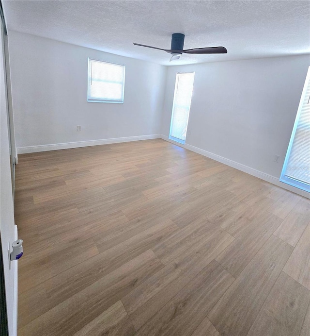 spare room featuring light wood-style flooring, a textured ceiling, baseboards, and a ceiling fan