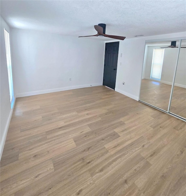 empty room featuring baseboards, a textured ceiling, light wood-style flooring, and a ceiling fan