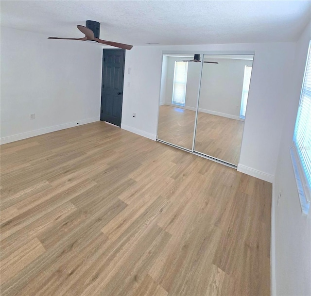 unfurnished bedroom featuring a textured ceiling, baseboards, light wood finished floors, and ceiling fan