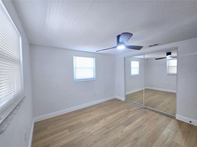 unfurnished bedroom with a ceiling fan, wood finished floors, visible vents, baseboards, and a closet