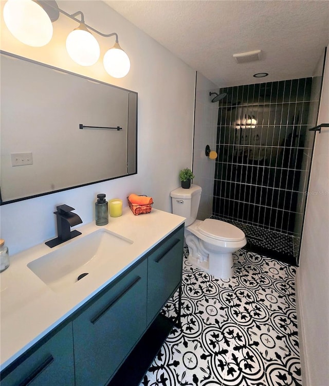 bathroom featuring vanity, visible vents, a tile shower, tile patterned flooring, and toilet