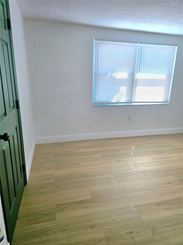 unfurnished room with light wood-type flooring, baseboards, and a textured ceiling