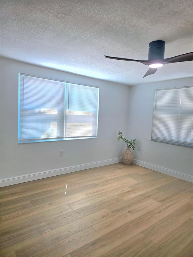 empty room featuring a textured ceiling, baseboards, a ceiling fan, and wood finished floors