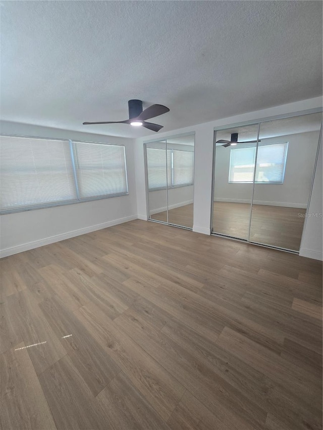 interior space with baseboards, multiple closets, a textured ceiling, and wood finished floors