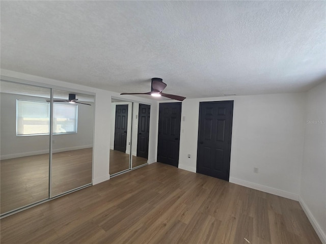 unfurnished bedroom with baseboards, wood finished floors, multiple closets, and a textured ceiling