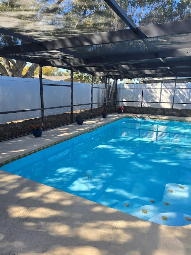 view of swimming pool featuring glass enclosure, a patio, a fenced backyard, and a fenced in pool