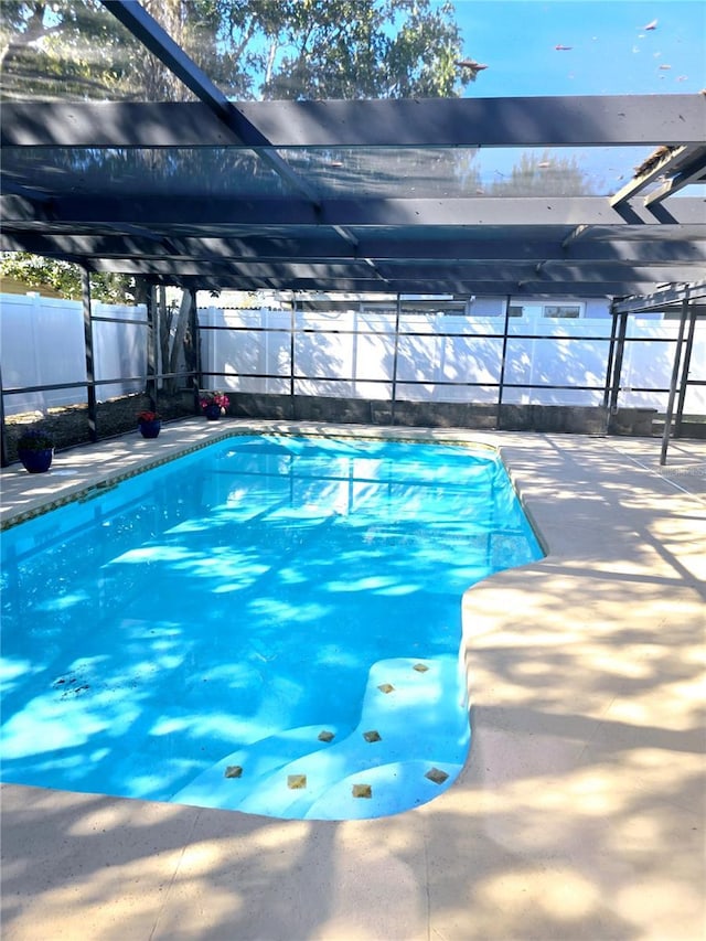 view of swimming pool featuring glass enclosure, a patio, a fenced in pool, and a fenced backyard