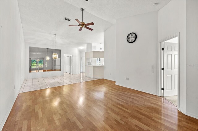 unfurnished living room with visible vents, ceiling fan with notable chandelier, a textured ceiling, and wood finished floors