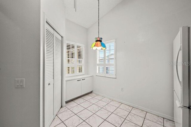 unfurnished dining area with vaulted ceiling, light tile patterned floors, baseboards, and a textured ceiling