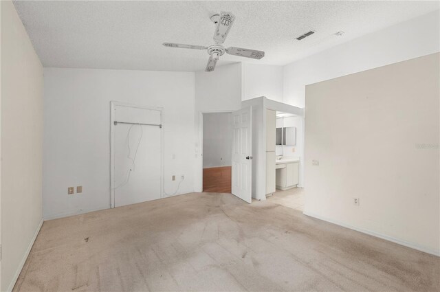 unfurnished bedroom with visible vents, ensuite bathroom, a textured ceiling, carpet flooring, and lofted ceiling