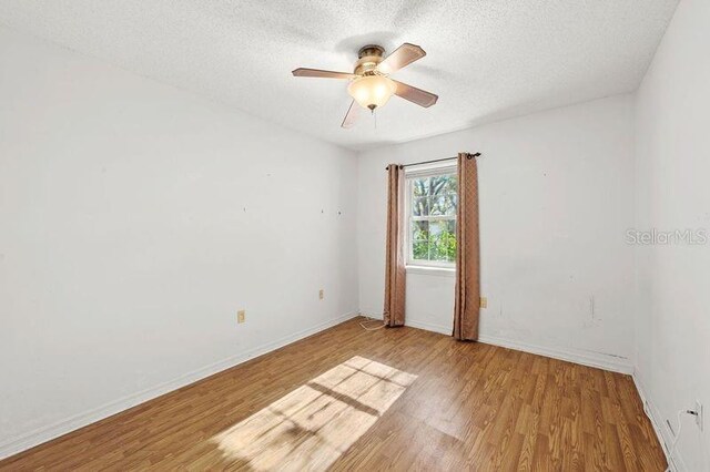 empty room featuring ceiling fan, baseboards, a textured ceiling, and light wood-style flooring