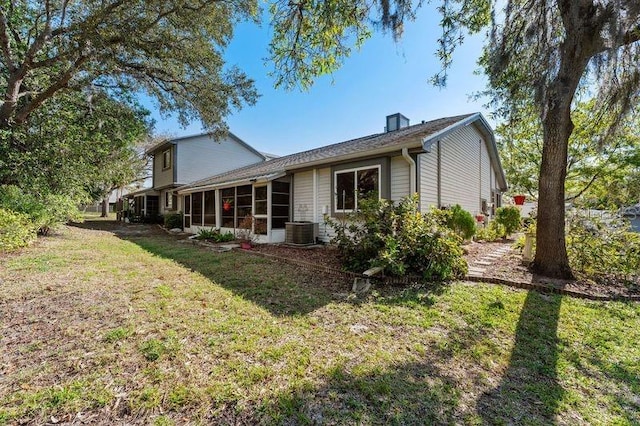 rear view of house featuring a yard, central AC unit, a sunroom, and a chimney