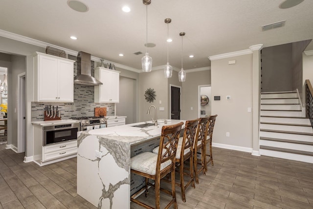 kitchen featuring visible vents, an island with sink, a sink, wall chimney exhaust hood, and stainless steel gas range