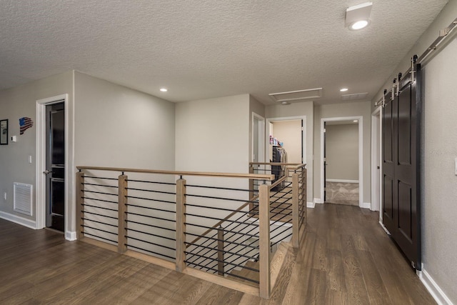 hallway featuring wood finished floors, visible vents, baseboards, a barn door, and an upstairs landing