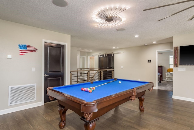 recreation room featuring visible vents, baseboards, a barn door, wood finished floors, and a textured ceiling