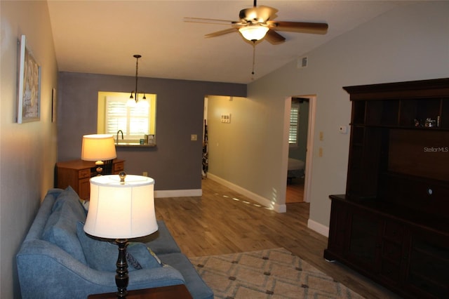 living area featuring visible vents, wood finished floors, baseboards, ceiling fan, and vaulted ceiling