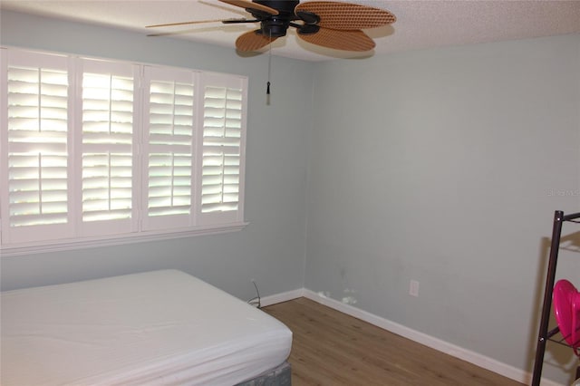 bedroom with ceiling fan, baseboards, a textured ceiling, and wood finished floors