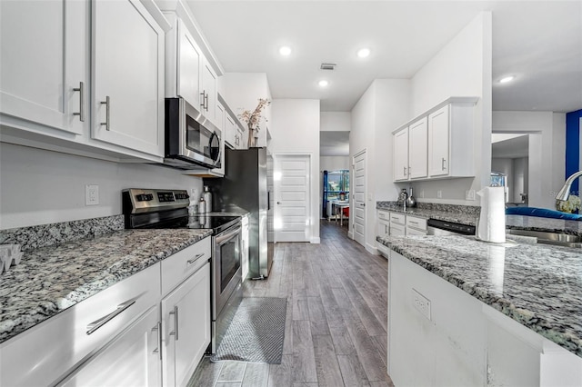 kitchen with visible vents, light stone counters, light wood-style flooring, appliances with stainless steel finishes, and white cabinetry