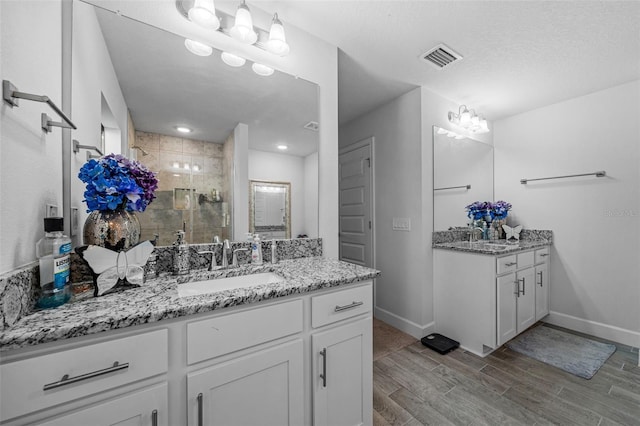 full bathroom featuring visible vents, two vanities, a stall shower, a sink, and wood tiled floor