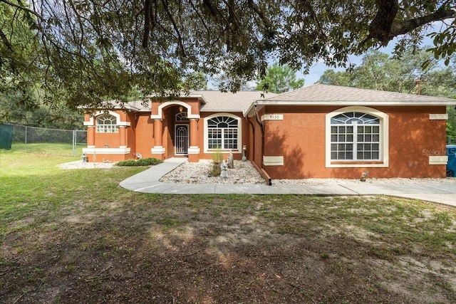 view of front facade with a shingled roof, a front yard, fence, and stucco siding