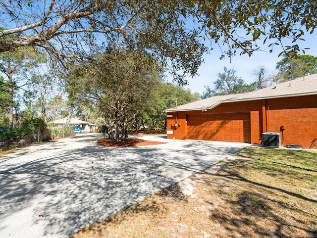 view of property exterior featuring a yard, an attached garage, central AC, and driveway