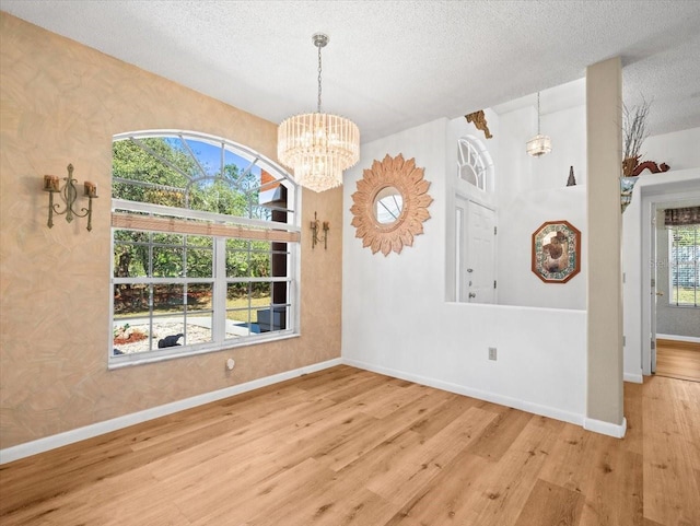 unfurnished dining area with baseboards, a textured ceiling, an inviting chandelier, and wood finished floors