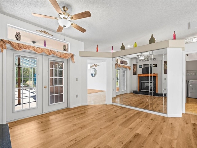 unfurnished living room featuring washer / clothes dryer, a textured ceiling, wood finished floors, a fireplace, and ceiling fan