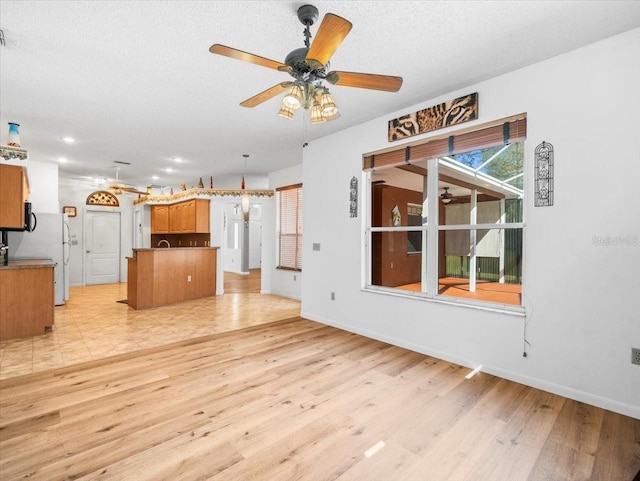 unfurnished living room with baseboards, light wood-style floors, ceiling fan, and a textured ceiling