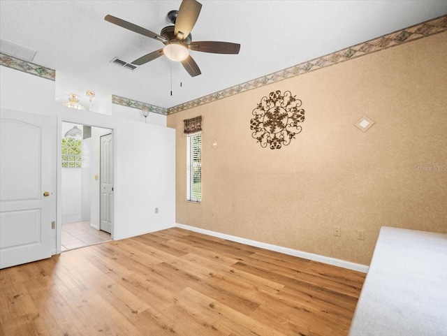 spare room with light wood-style floors, a ceiling fan, visible vents, and baseboards