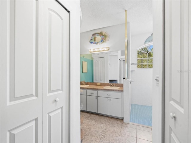 full bath with double vanity, a sink, tile patterned flooring, a closet, and a textured ceiling