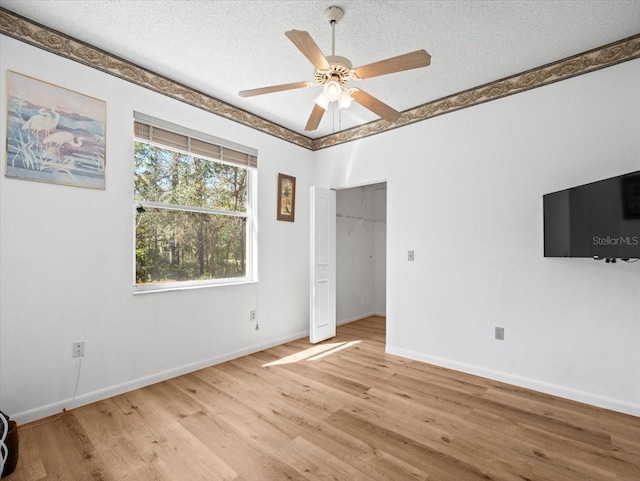 interior space featuring light wood-style flooring, a ceiling fan, baseboards, and a textured ceiling