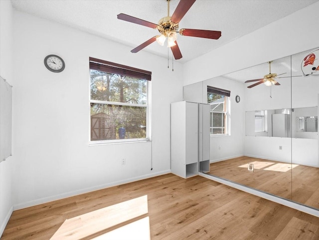 unfurnished bedroom featuring multiple windows, a ceiling fan, baseboards, and wood finished floors