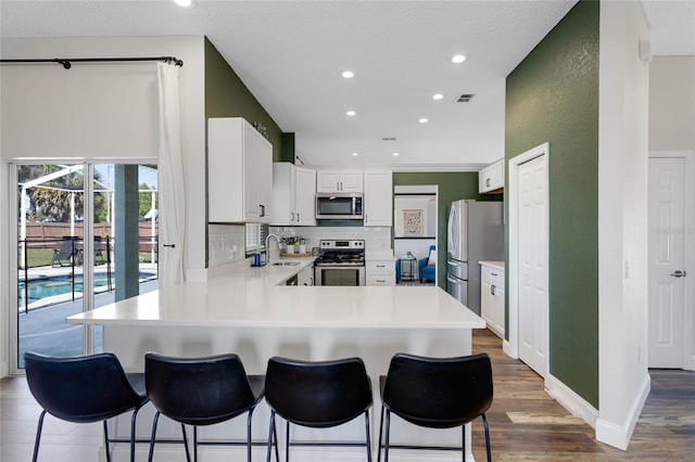 kitchen featuring a peninsula, a sink, light countertops, appliances with stainless steel finishes, and tasteful backsplash