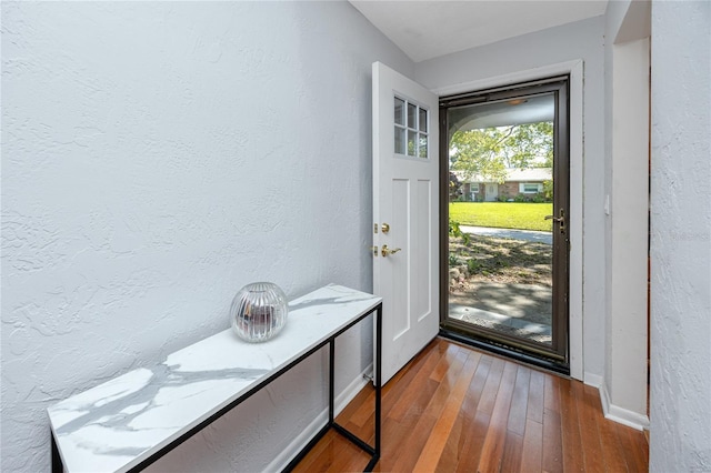 doorway featuring hardwood / wood-style flooring, a textured wall, and baseboards