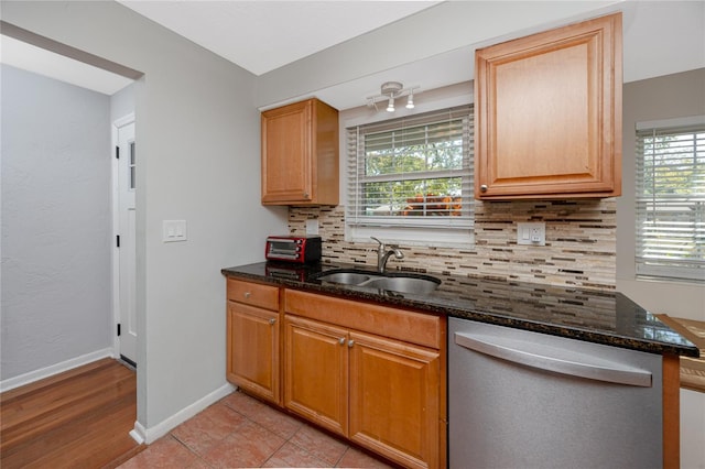 kitchen with backsplash, baseboards, dishwasher, dark stone countertops, and a sink