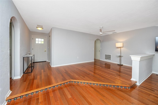 interior space featuring visible vents, a ceiling fan, hardwood / wood-style floors, arched walkways, and baseboards