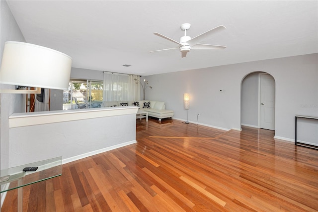 unfurnished living room with baseboards, arched walkways, wood finished floors, and a ceiling fan