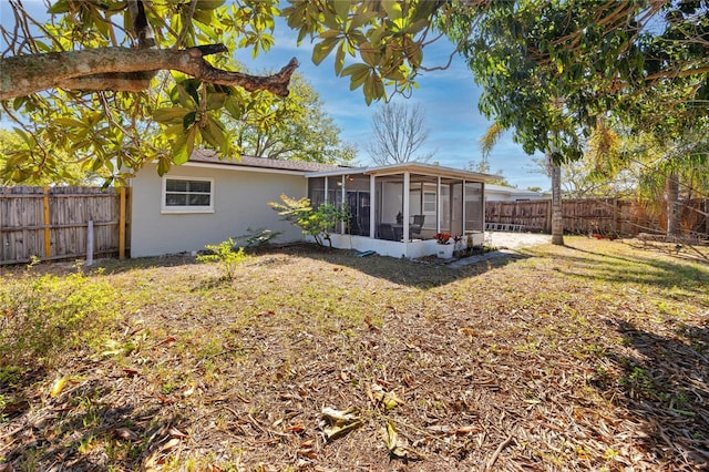 back of house with a fenced backyard, a sunroom, and stucco siding