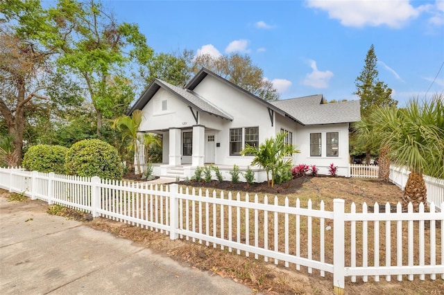 view of front of house with a shingled roof, a fenced front yard, and stucco siding